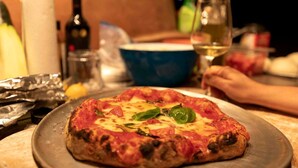 A pizza on a metal plate with a table setting in the background. - Cardinal's Inn Cabin Rental in Nova Scotia (Baddeck)