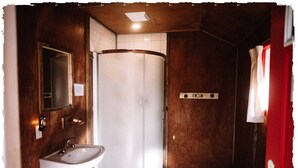 A bathroom with a shower, a sink, a mirror, and a red curtain.