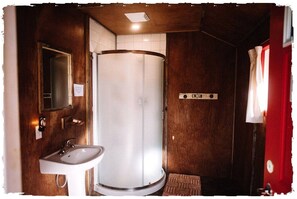 A bathroom with a shower, a sink, a mirror, and a red curtain.