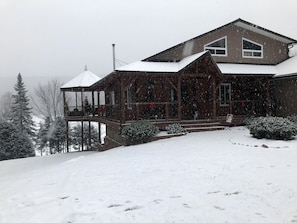 A wooden house with a covered porch and a snow-covered landscape.