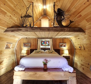 Ein Schlafzimmer einer Holzhütte mit einem Bett, Nachttischlampen, einem Fenster und einer dekorativen Fischskulptur.
