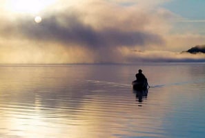 A person in a boat on calm water with a sunrise or sunset in the background. - Secluded Rental Perfect for a Romantic Getaway in Algonquin Park, Ontario (South River)