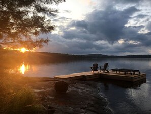 A wooden dock extending into a calm lake with a sunset in the background.