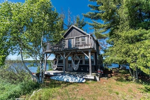 A wooden cabin with a balcony, a hammock, and a view of the lake.