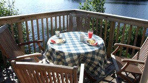 Eine Terrasse mit kariertem Tischläufer, Holzkästen und einem Tisch, gedeckt mit Tellern, einer Karaffe und einem Glas rosa Getränk.