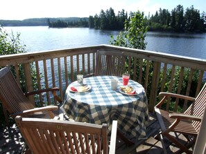 A deck with a checkered tablecloth, wooden chairs, and a table set with plates, a pitcher, and a glass of pink beverage.