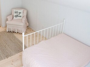A room with a white metal bed frame, a beige chair with a cushion, and a patterned rug. - Lakefront Chalet in Prince Edward County (Prince Edward County)