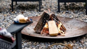 Ein Lagerfeuer mit Holzscheiten, umgeben von Stühlen und einem Tisch mit einer Decke.