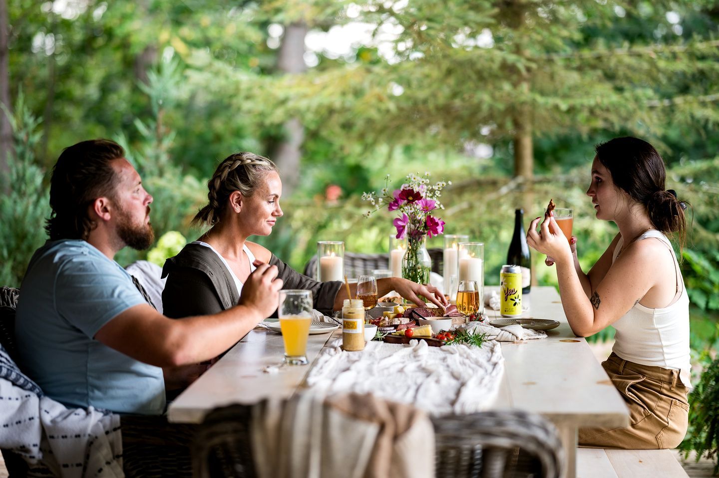 Eine Gruppe von Menschen speist im Freien an einem Tisch mit Essen, Getränken und Kerzen.