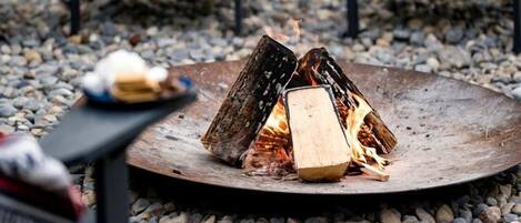 A fire pit with logs, surrounded by chairs and a table with a blanket.