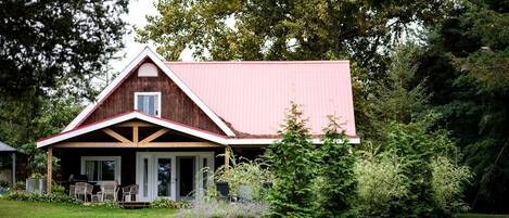 A rustic barn-style building with a red roof, a porch with chairs, and a well-maintained lawn.
