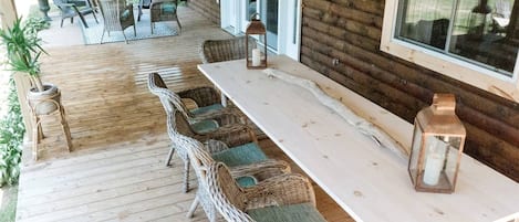 A covered patio with wicker furniture, a long table, and lanterns.