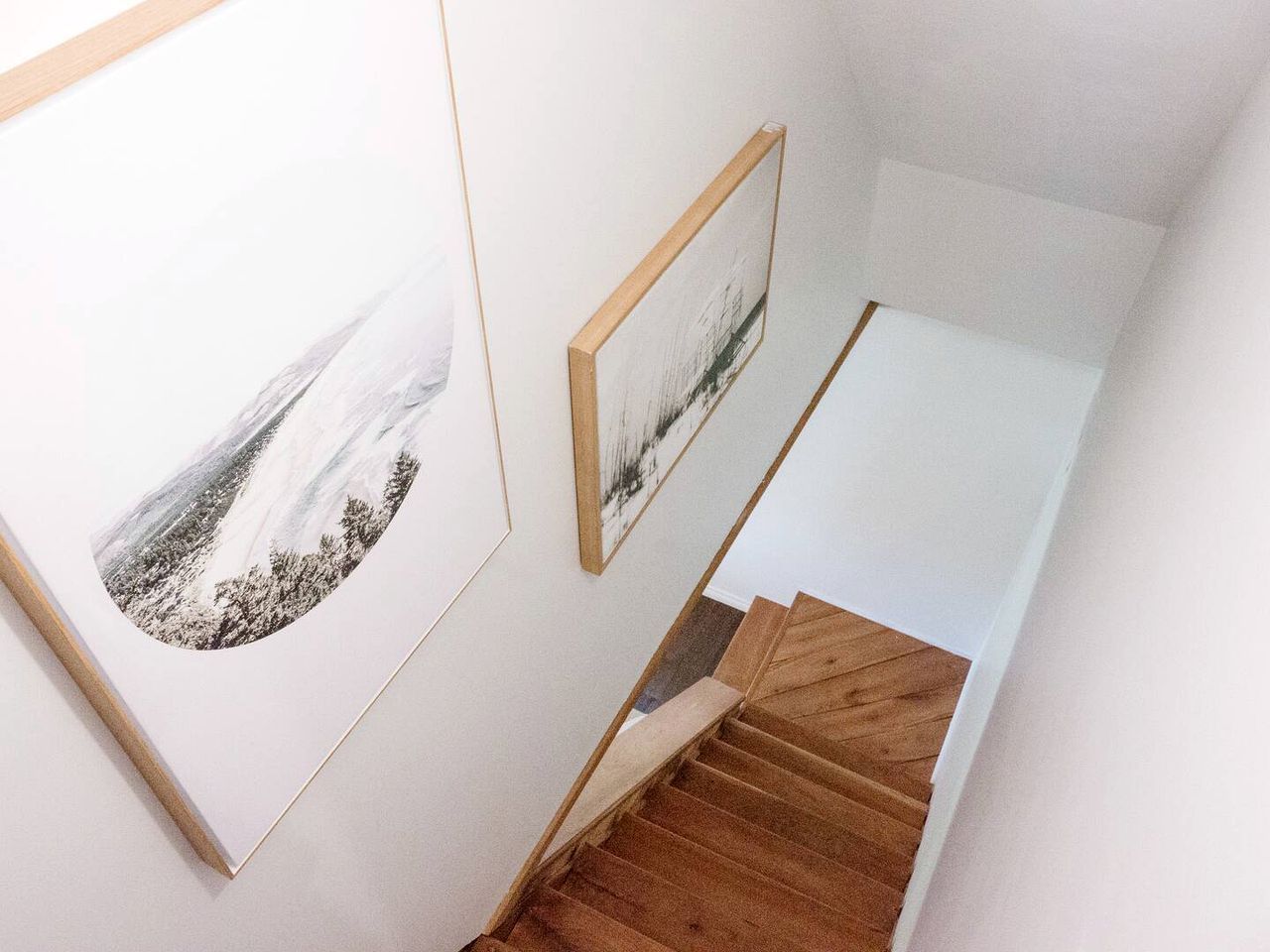 A staircase with wooden steps and a white landing area, flanked by framed artwork on the walls.
