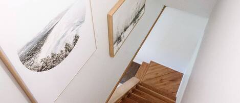 A staircase with wooden steps and a white landing area, flanked by framed artwork on the walls.