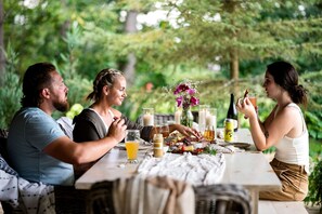 Eine Gruppe von Menschen speist im Freien an einem Tisch mit Essen, Getränken und Kerzen.