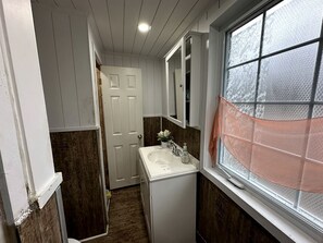 A narrow bathroom with a white sink, a mirror, and a window with frosted glass.