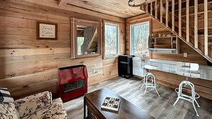 A cabin interior with a wooden floor, a sofa, a red cabinet, a table with a game, and a staircase. - Cozy Secluded Tiny Cabin for a True Getaway in the Outdoors Surrounded by Nature in Simcoe, Ontario (Simcoe)