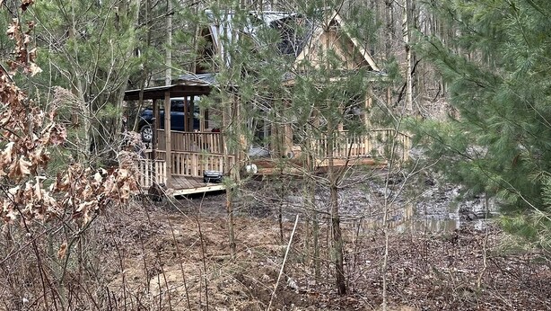 A cabin with a deck, surrounded by trees and a small stream. - Cozy Secluded Tiny Cabin for a True Getaway in the Outdoors Surrounded by Nature in Simcoe, Ontario (Simcoe)
