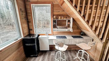 A compact kitchen with a wooden countertop, two bar stools, a sink, and a window with a view of trees.