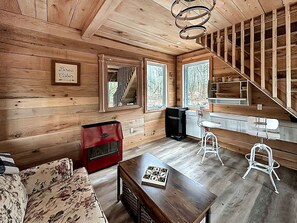 A cabin interior with a wooden floor, a sofa, a red cabinet, a table with a game, and a staircase.