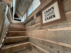 A wooden cabin interior with a staircase, wooden walls, and a sign that reads 'CABIN Sweet Cabin.' - Cozy Secluded Tiny Cabin for a True Getaway in the Outdoors Surrounded by Nature in Simcoe, Ontario (Simcoe)