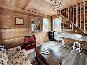 A cabin interior with a wooden floor, a sofa, a red cabinet, a table with a game, and a staircase.