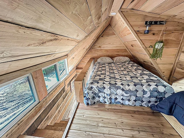 A wooden cabin interior with a bed, wooden walls, and a window with a view.