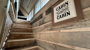 A wooden cabin interior with a staircase, wooden walls, and a sign that reads 'CABIN Sweet Cabin.' - Cozy Secluded Tiny Cabin for a True Getaway in the Outdoors Surrounded by Nature in Simcoe, Ontario (Simcoe)