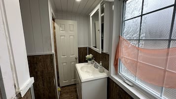 A narrow bathroom with a white sink, a mirror, and a window with frosted glass.