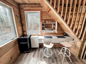 A compact kitchen with a wooden countertop, two bar stools, a sink, and a window with a view of trees.