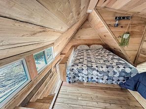 A wooden cabin interior with a bed, wooden walls, and a window with a view.