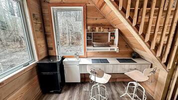 A compact kitchen with a wooden countertop, two bar stools, a sink, and a window with a view of trees.