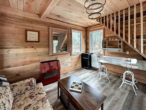 Interior de una cabaña con suelo de madera, un sofá, un armario rojo, una mesa con un juego y una escalera.