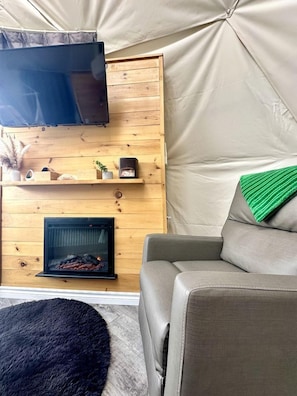 Un espace de vie chaleureux avec une cheminée, un canapé, un téléviseur et une structure ressemblant à une tente.