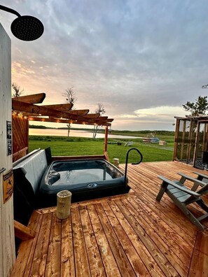 Ein Whirlpool auf einer Holzterrasse mit Blick auf einen See und Wiesen.