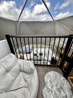 A tented room with a view of a dock and boat, a cushioned seating area, and a furry rug.