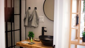 Een badkamer met een houten wastafelmeubel, een zwarte wastafel, een spiegel en handdoeken aan haken.