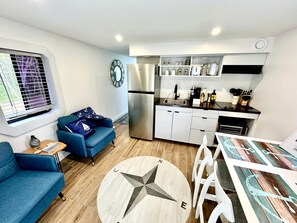 A compact living space with a kitchenette, a dining area, a sofa, and a round table with a compass design.