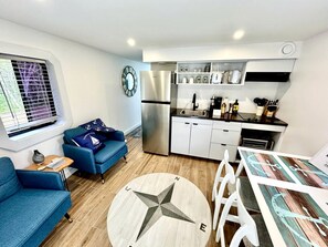 A compact living space with a kitchenette, a dining area, a sofa, and a round table with a compass design. - Peaceful Boat Retreat with Luxury Interior with Hot Tub in Cocagne, New Brunswick (Cocagne)
