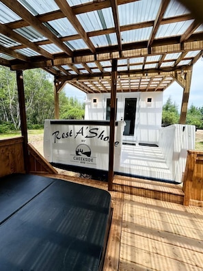 A wooden deck with a covered seating area, a small white building labeled 'Rest A' Shop,' and a natural outdoor setting.