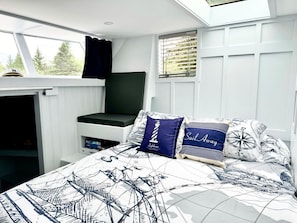 Une chambre à coucher avec un lit, une fenêtre avec des rideaux, une banquette intégrée et un puits de lumière.