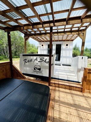 A wooden deck with a covered seating area, a small white building labeled 'Rest A' Shop,' and a natural outdoor setting. - Peaceful Boat Retreat with Luxury Interior with Hot Tub in Cocagne, New Brunswick (Cocagne)