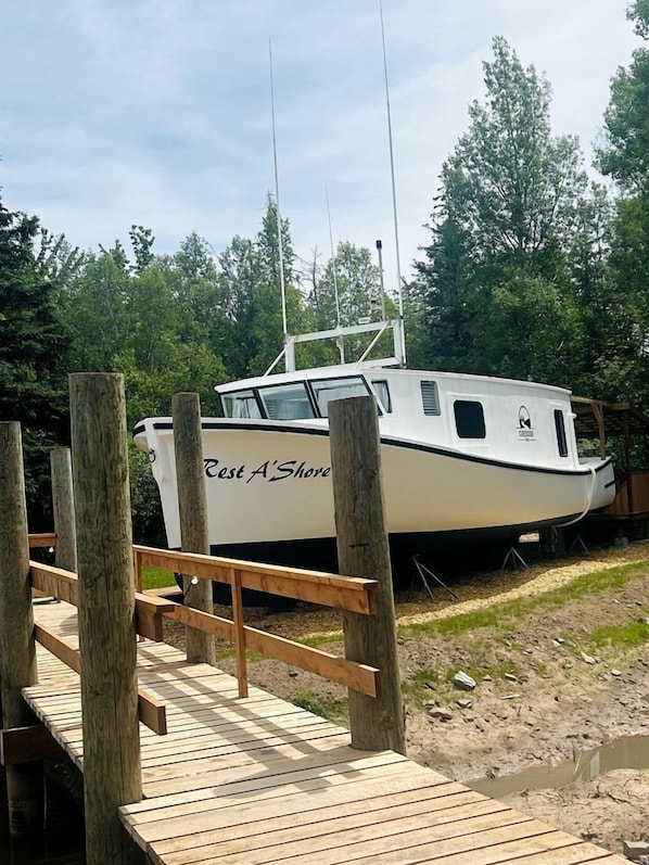 Un bateau blanc, baptisé « East A’Shore », était amarré à un quai en bois, avec une forêt en arrière-plan.