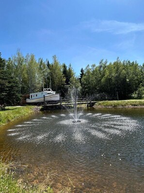 A boat docked near a pond with a fountain, surrounded by trees.