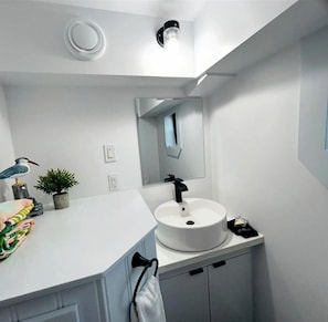 Une salle de bain moderne avec un lavabo blanc, un miroir et un luminaire fixé au plafond.