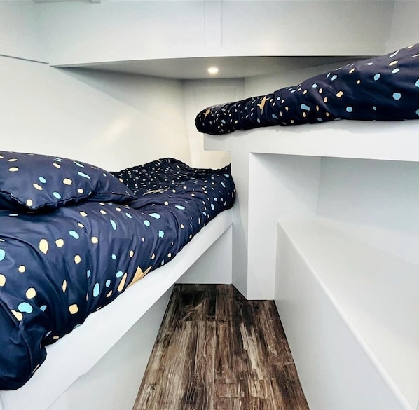 A compact room with two bunk beds, each with a polka dot duvet.