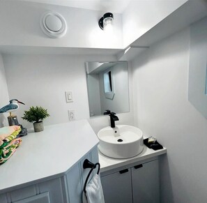 A modern bathroom with a white sink, a mirror, and a ceiling light fixture.
