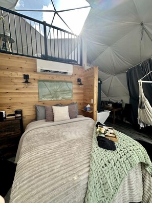 A tented room with a bed, a small desk, a hanging chair, and a window with a view. - Getaways to the Canadian Countryside in this Lovely Dome Rental in Nova Scotia (Antigonish)