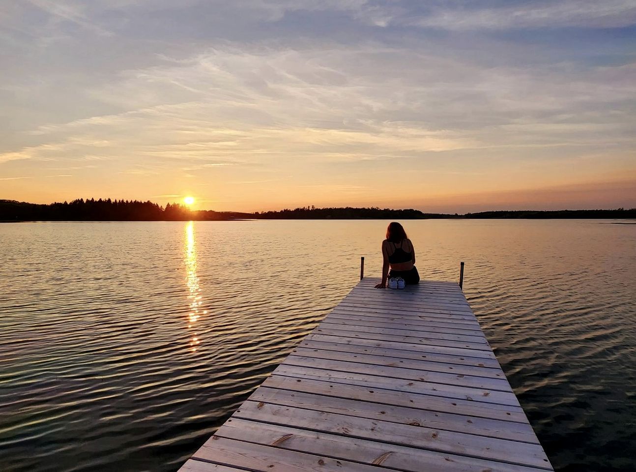 A wooden pier extending into calm water with a sunset in the background.