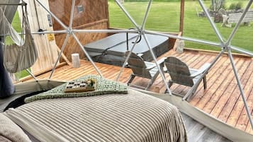 Un hébergement sous tente comprenant un lit, une table et des chaises, et offrant une vue sur une zone herbeuse.
